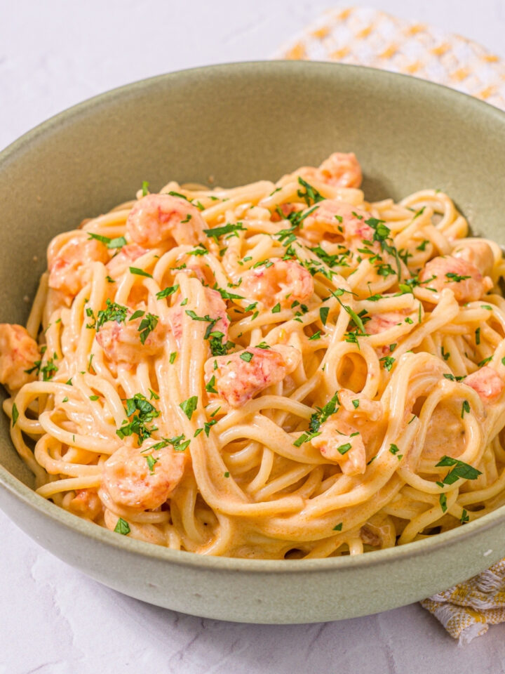 A bowl of Trader Joe's lobster bisque pasta garnished with fresh parsley. The bowl is on a marble counter with a yellow striped napkin.