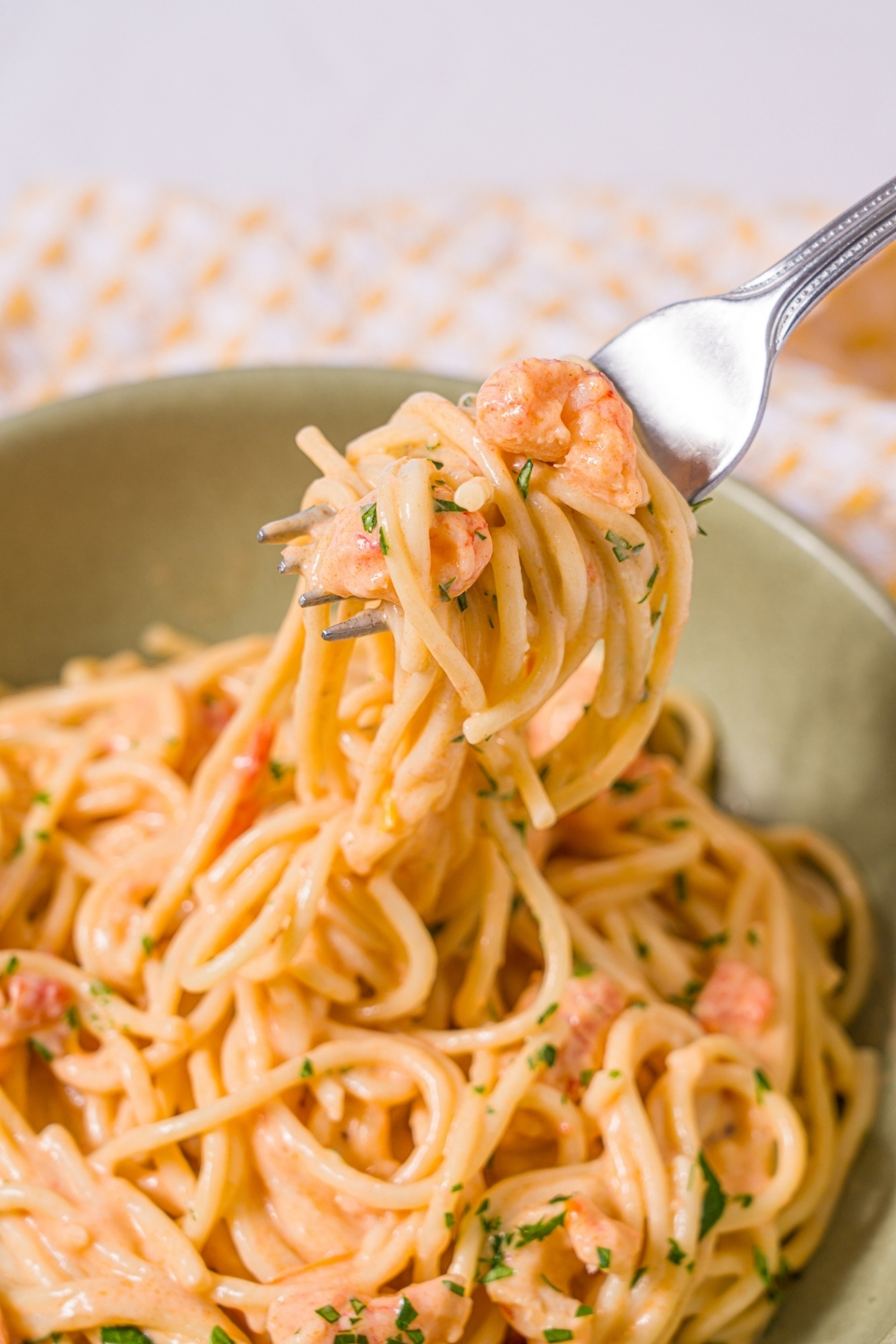 A bowl of Trader Joe's lobster bisque pasta garnished with fresh parsley. A fork is taking a bite of the pasta. The bowl is on a marble counter with a yellow striped napkin.