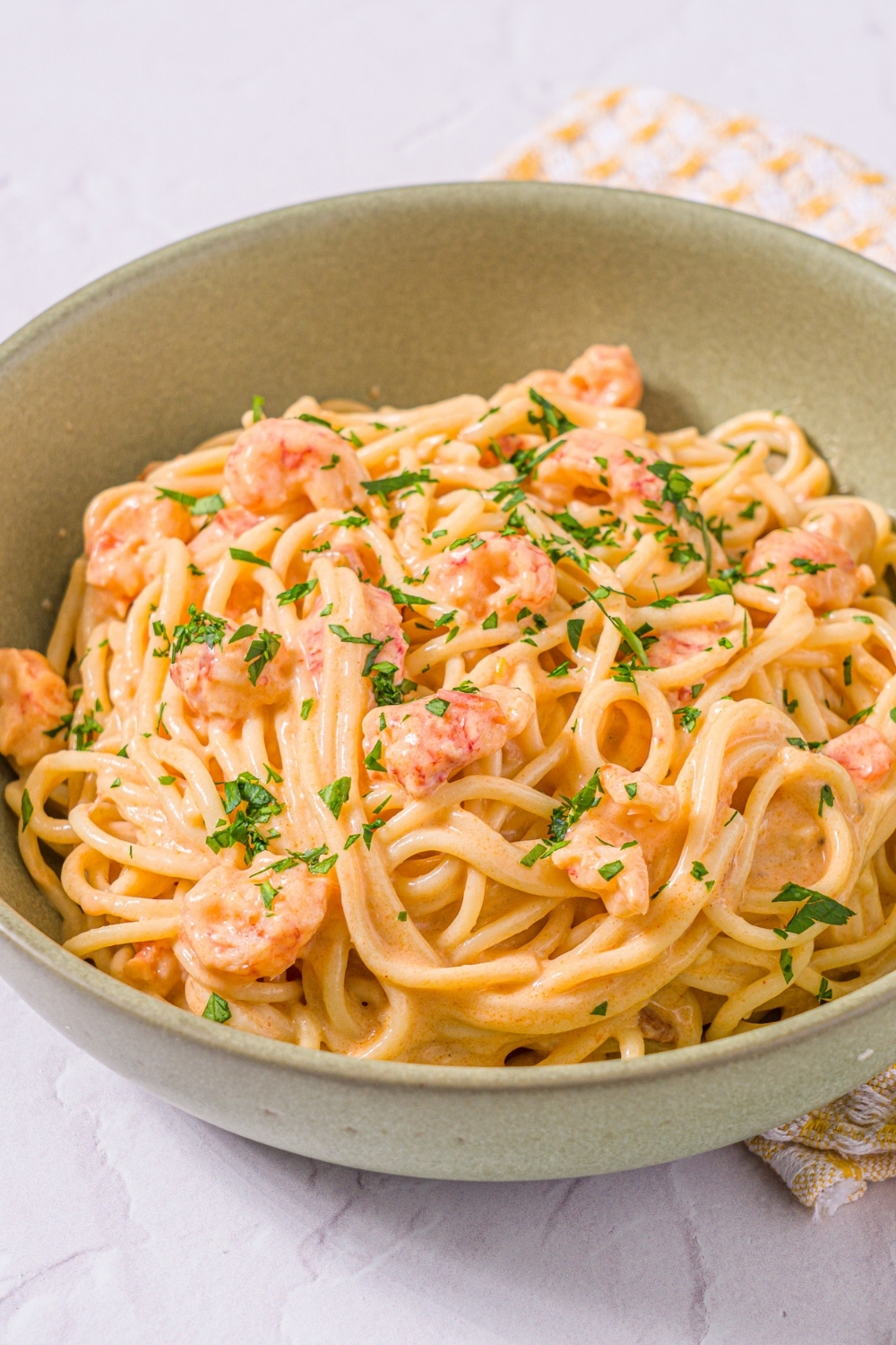 A bowl of Trader Joe's lobster bisque pasta garnished with fresh parsley. The bowl is on a marble counter with a yellow striped napkin.
