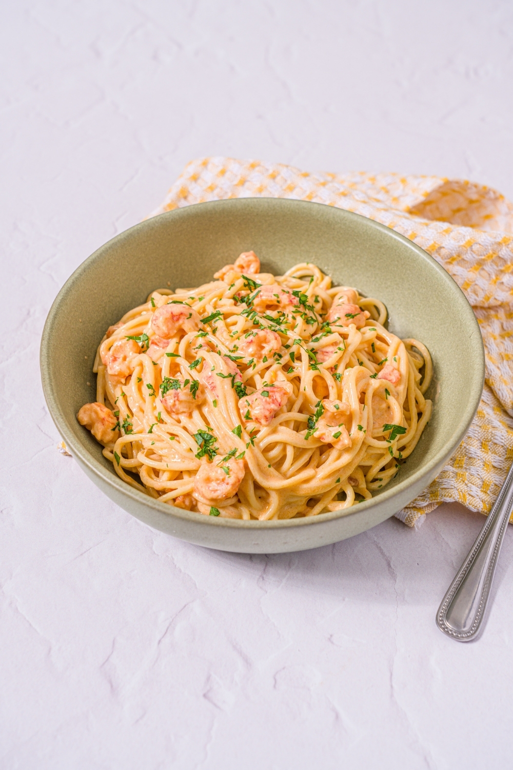 A bowl of Trader Joe's lobster bisque pasta garnished with fresh parsley. A fork is taking a bite of the pasta. The bowl is on a marble counter with a yellow striped napkin and a fork.
