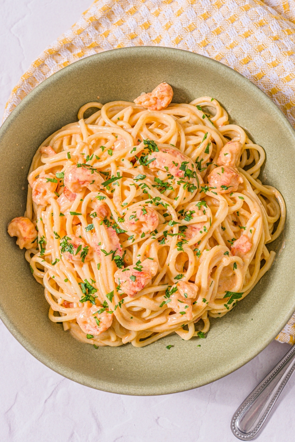 A bowl of Trader Joe's lobster bisque pasta garnished with fresh parsley. The bowl is on a marble counter with a yellow striped napkin and a fork.