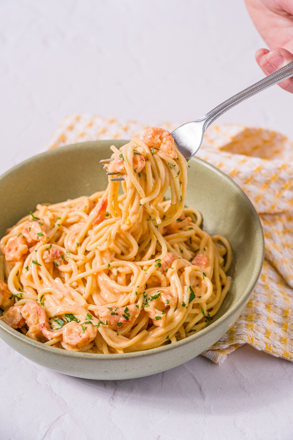 A bowl of Trader Joe's lobster bisque pasta garnished with fresh parsley. A fork is taking a bite of the pasta. The bowl is on a marble counter with a yellow striped napkin.