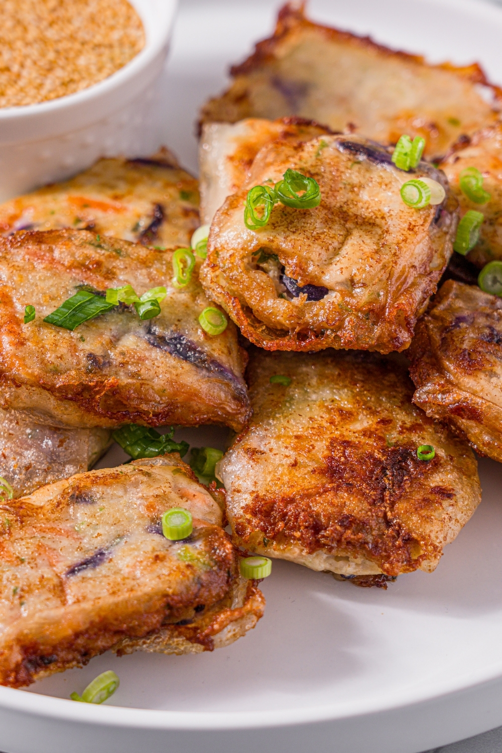 A white plate with chicken and shrimp rice paper dumplings garnished with sliced green onions and served with a small bowl of dipping sauce. The plate is on a marble counter.