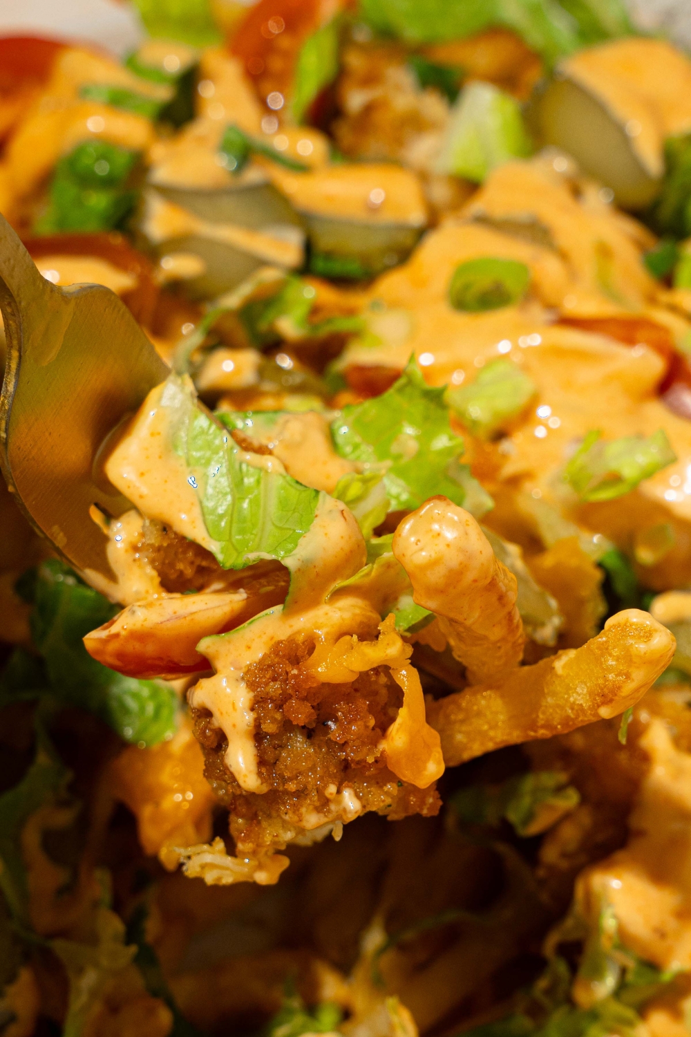 A close up of a fork taking a bite of chicken burger bowl loaded fries including crispy chicken, lettuce, fries, melted cheese, and burger sauce.