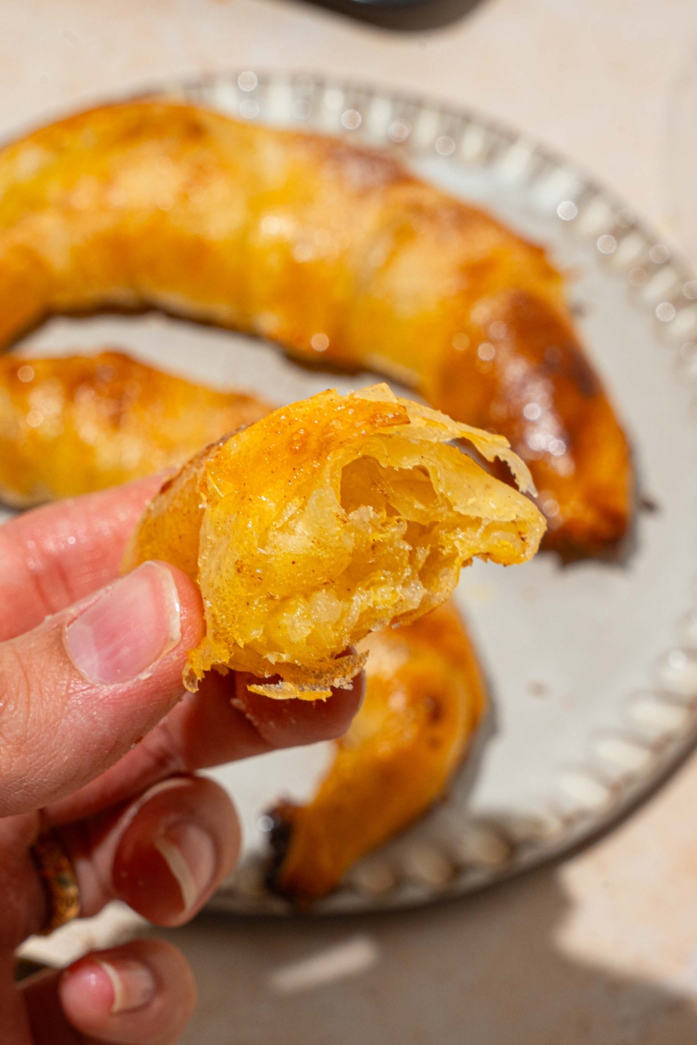 A close up of a hand holding a rice paper croissant sliced in half. There is a plate of croissants on a tan counter blurred in the background.