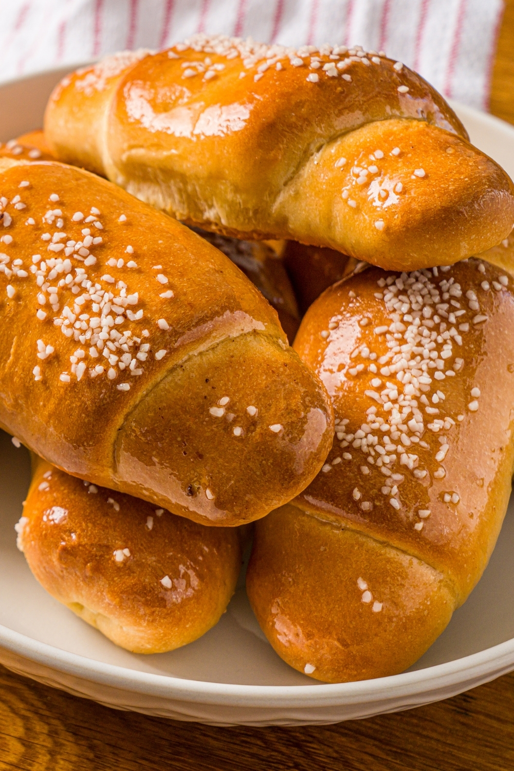 A white bowl with a pile of salt bread. The bowl is on a wooden counter with a red striped napkin.