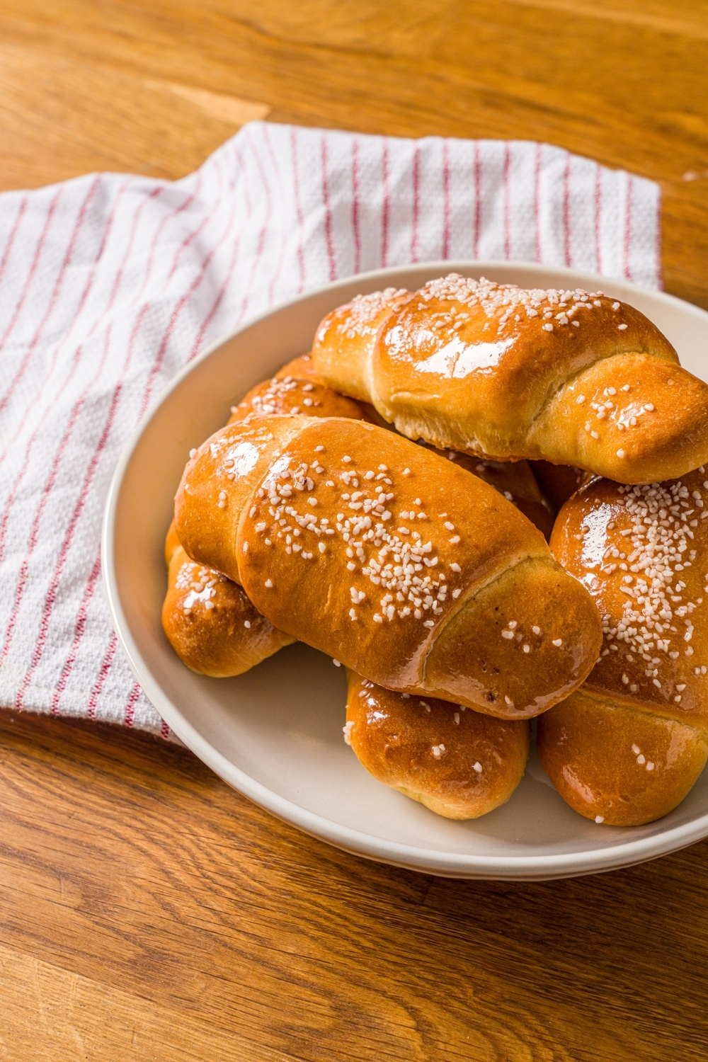 A white bowl with a pile of salt bread. The bowl is on a wooden counter with a red striped napkin.