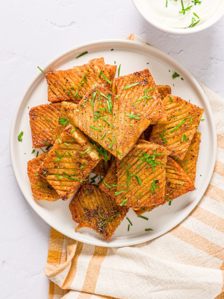 A bunch of accordion potatoes stacked on top of one another on a white plate.