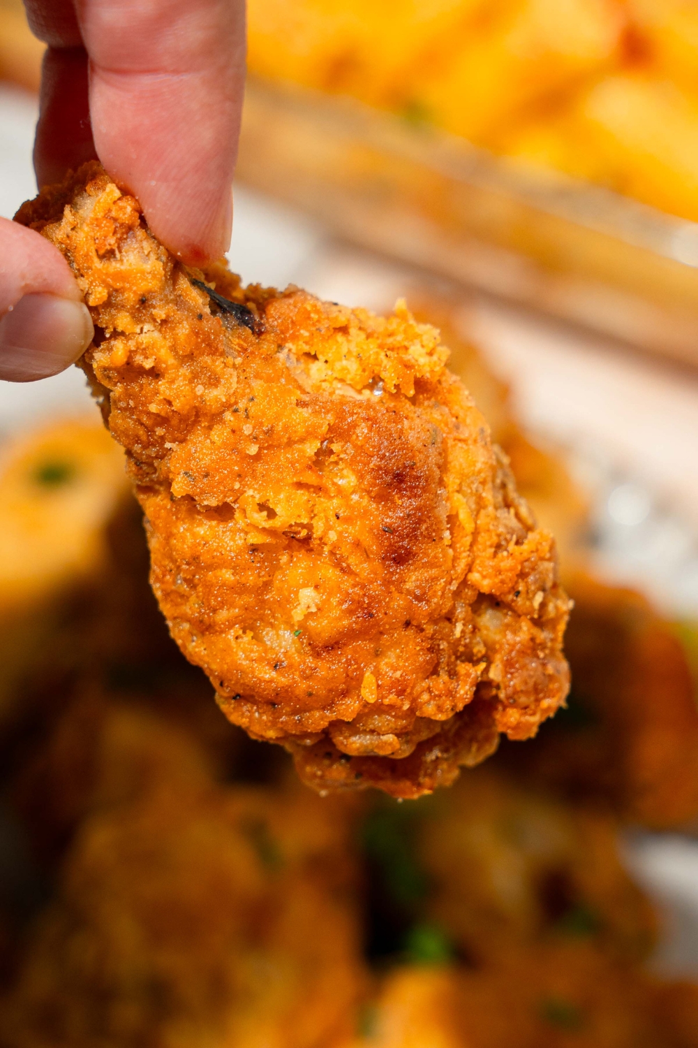 A close up of a crispy fried wing with a plate of wings blurred in the background.