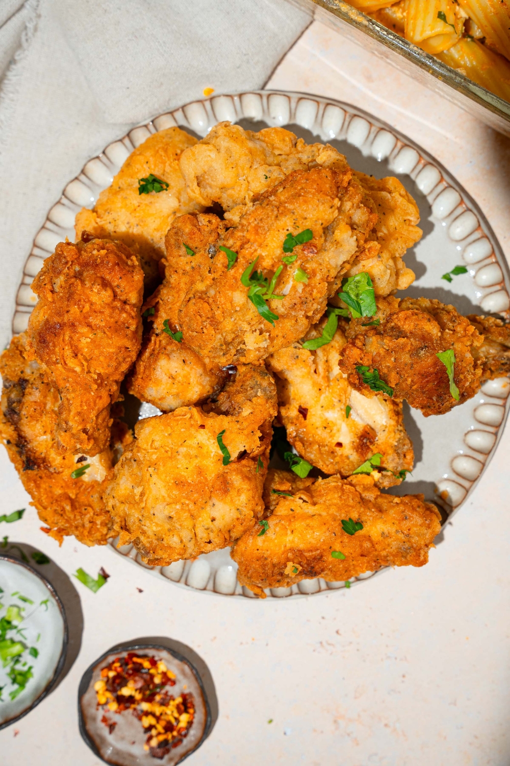 A plate with crispy fried chicken wings garnished with fresh parsley. The plate is on a tan counter with small bowls of garnishes.