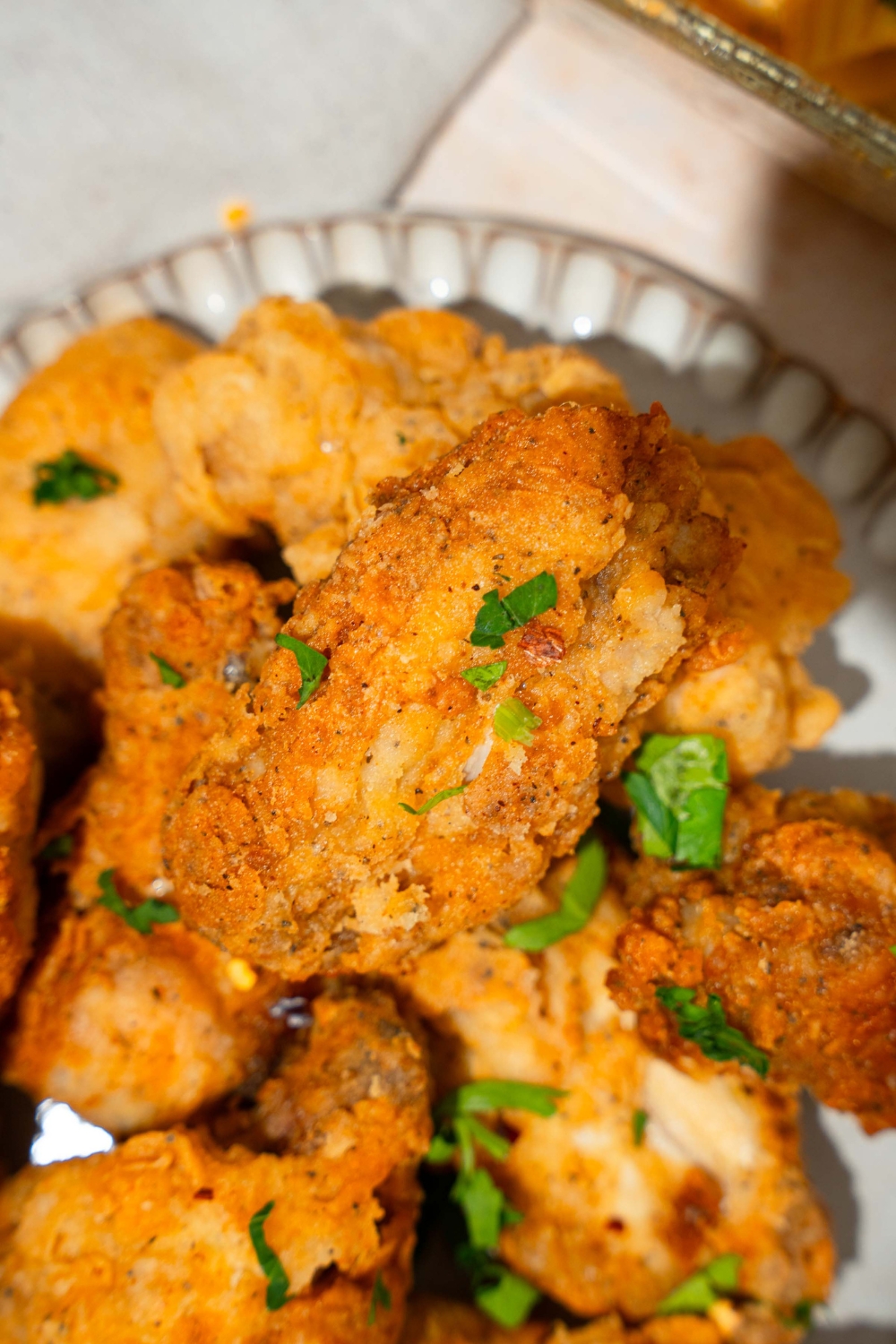 A plate with crispy fried chicken wings garnished with fresh parsley. The plate is on a tan counter.