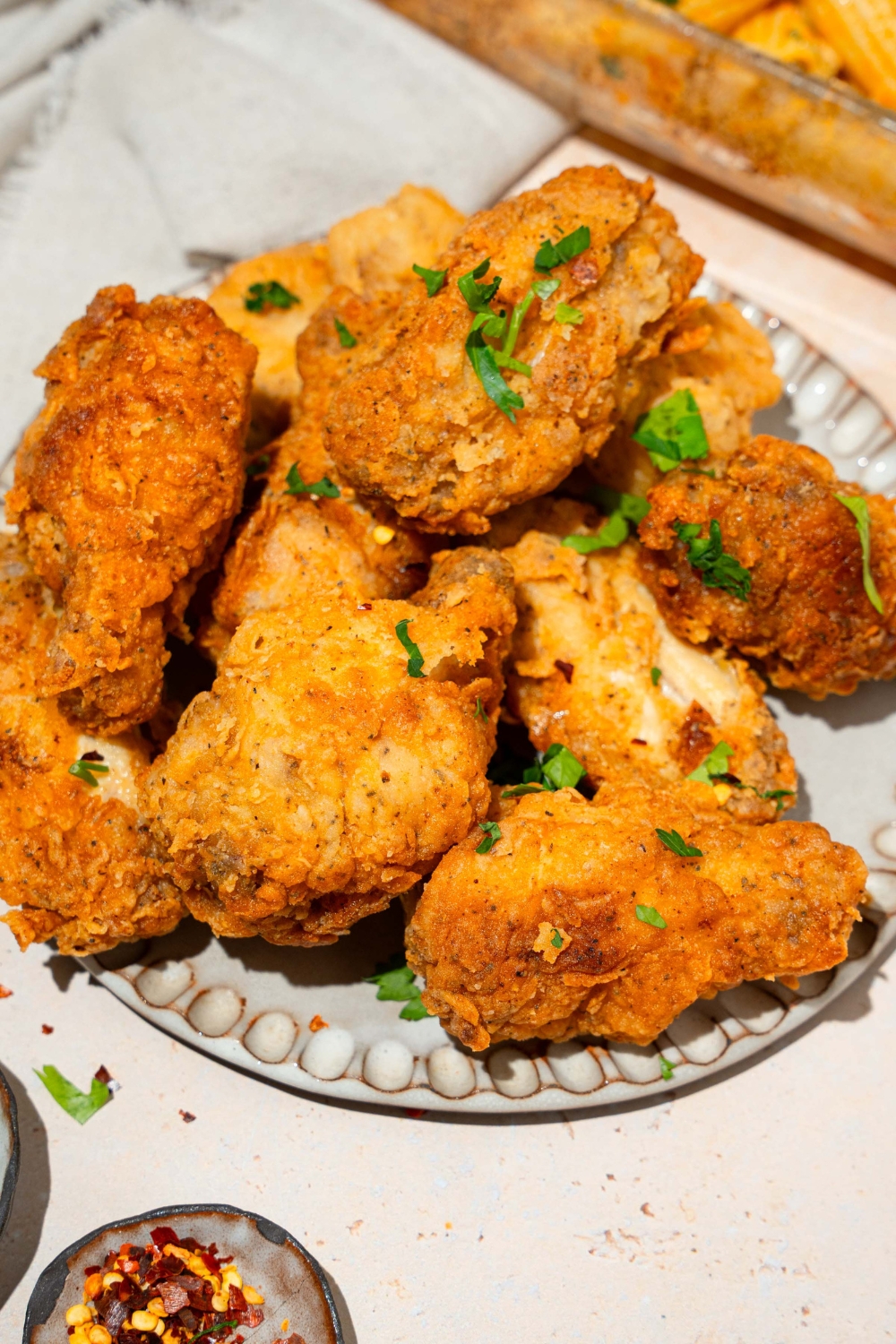 A plate with crispy fried chicken wings garnished with fresh parsley. The plate is on a tan counter with small bowls of garnishes.