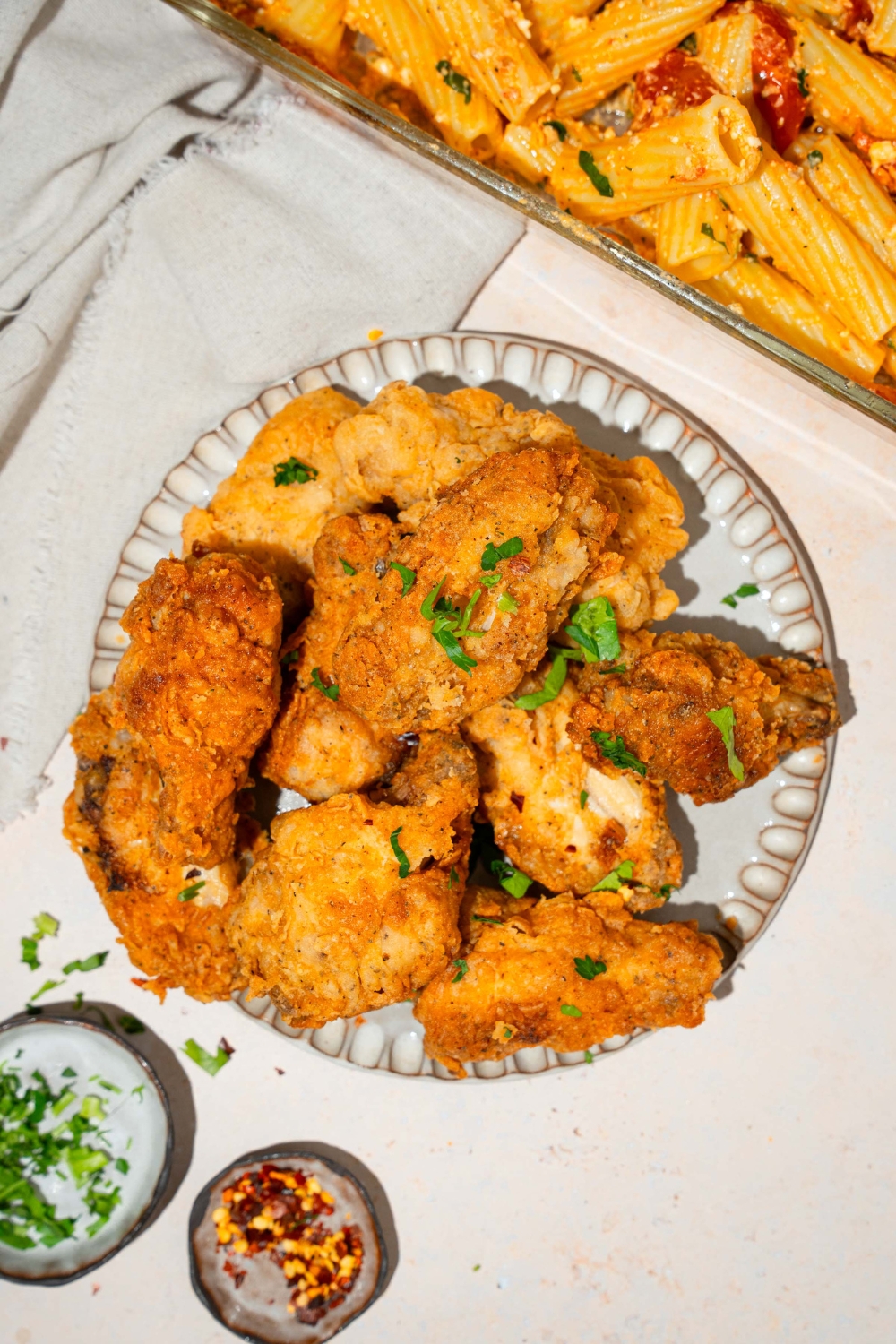 A plate with crispy fried chicken wings garnished with fresh parsley. The plate is on a tan counter with small bowls of garnishes.