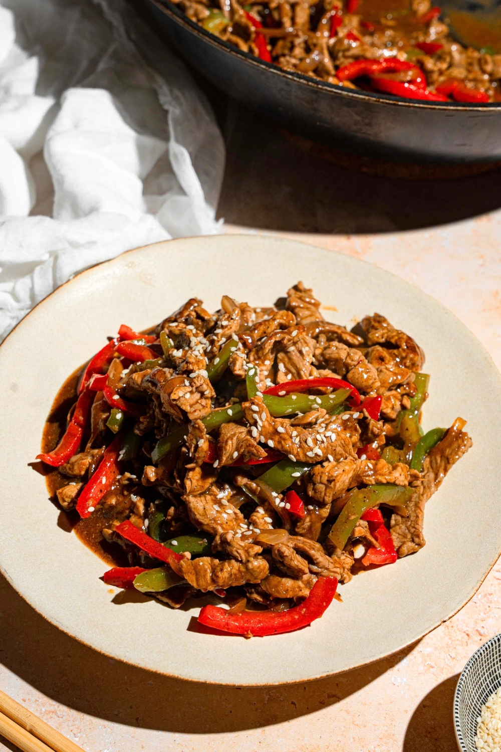 A bunch of pieces of sliced flank steak and red and green bell peppers and onions coated in a stir fry sauce on a white plate.