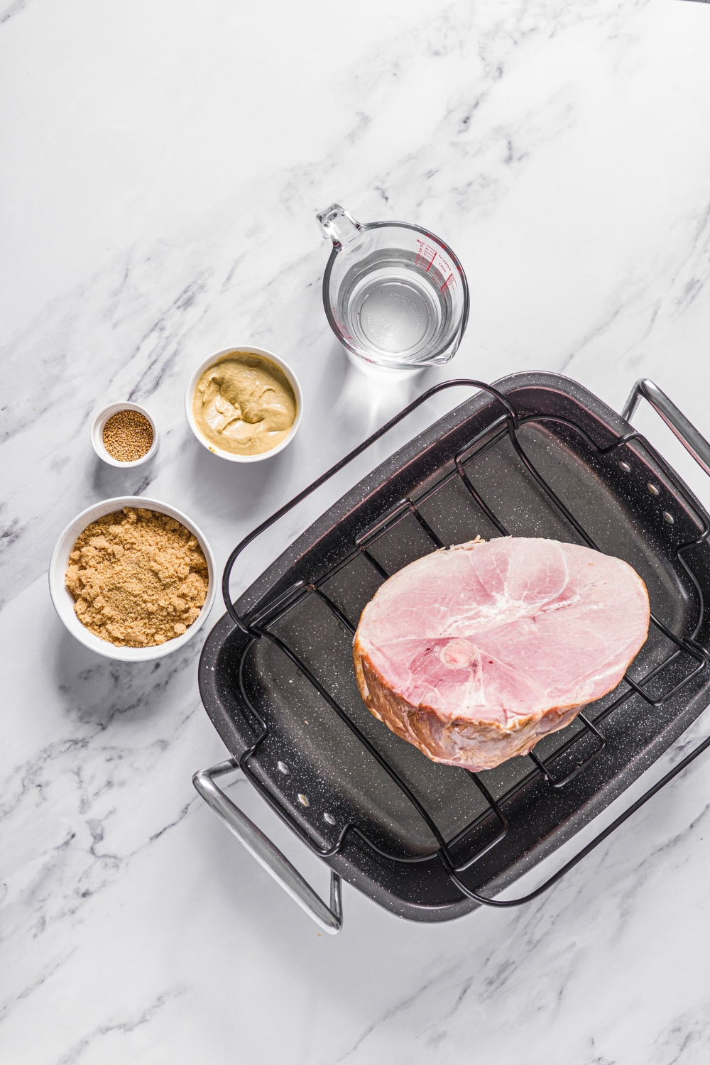A handshake and a roasting pan, a bowl of Dijon, mustard, bowl, brown sugar, a bowl of mustard, seeds, and a picture of water on a gray counter.
