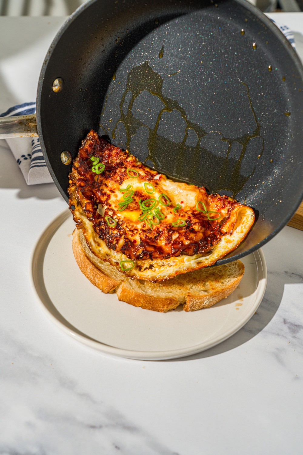 A skillet sliding hot honey eggs onto a piece of sourdough toast that is on a white plate.