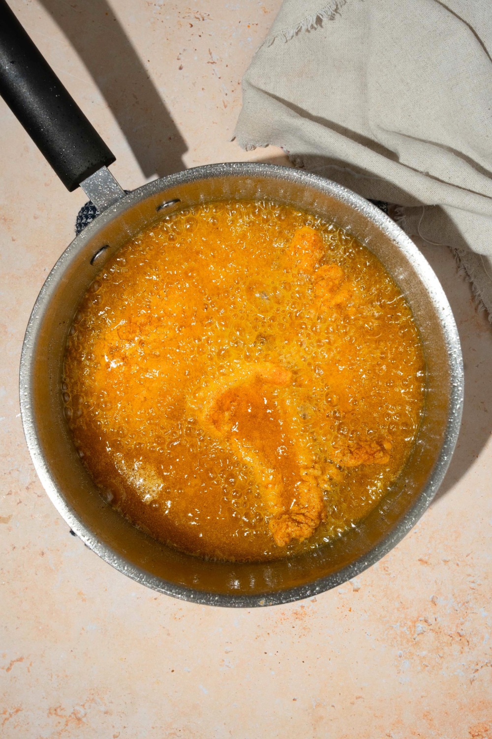 A piece of breaded whiting fish in a pot of bubbling oil.