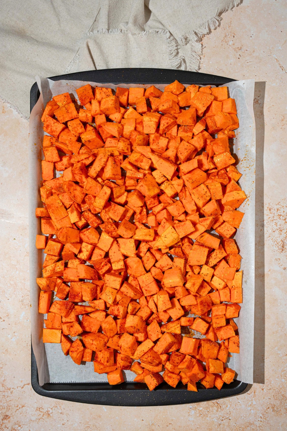 A bunch of diced roasted sweet potatoes on a sheet of parchment paper on a baking sheet.