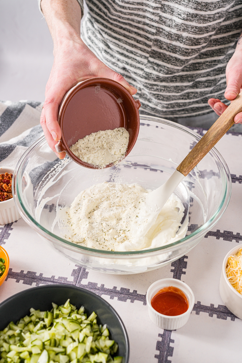 A hand pouring cream cheese into a glass bowl that has a creamy mixture in it.