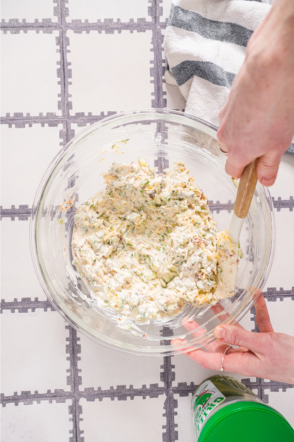 A hand holding a rubber spatula folding together creamy Grillo's pickle dip.