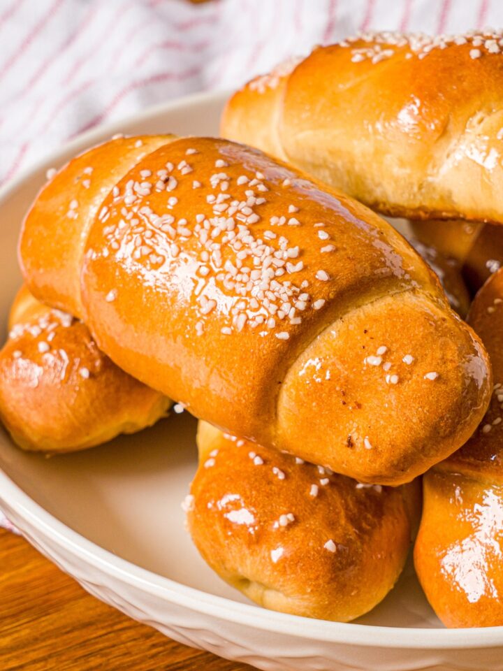 A piece of salt bread on top of a few more pieces of salt bread on a white plate.