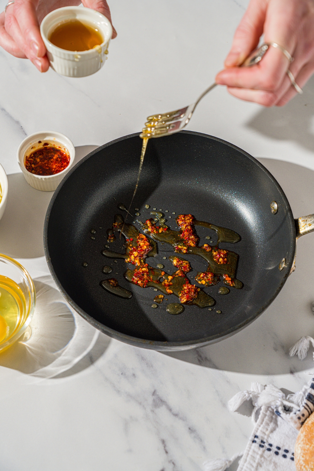 A hand holding a fork drizzling honey into a skillet that has chili crisps in it to make hot honey eggs.