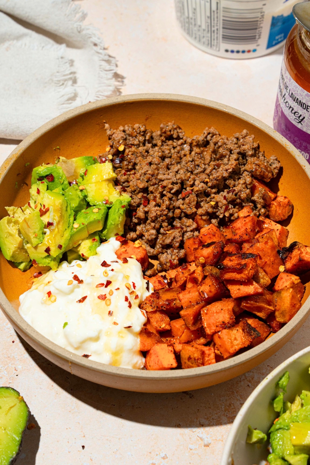 A sweet potato ground beef bowl that has seasoned ground beef, diced, roasted sweet potatoes, cottage cheese, and sliced avocado in a bowl.