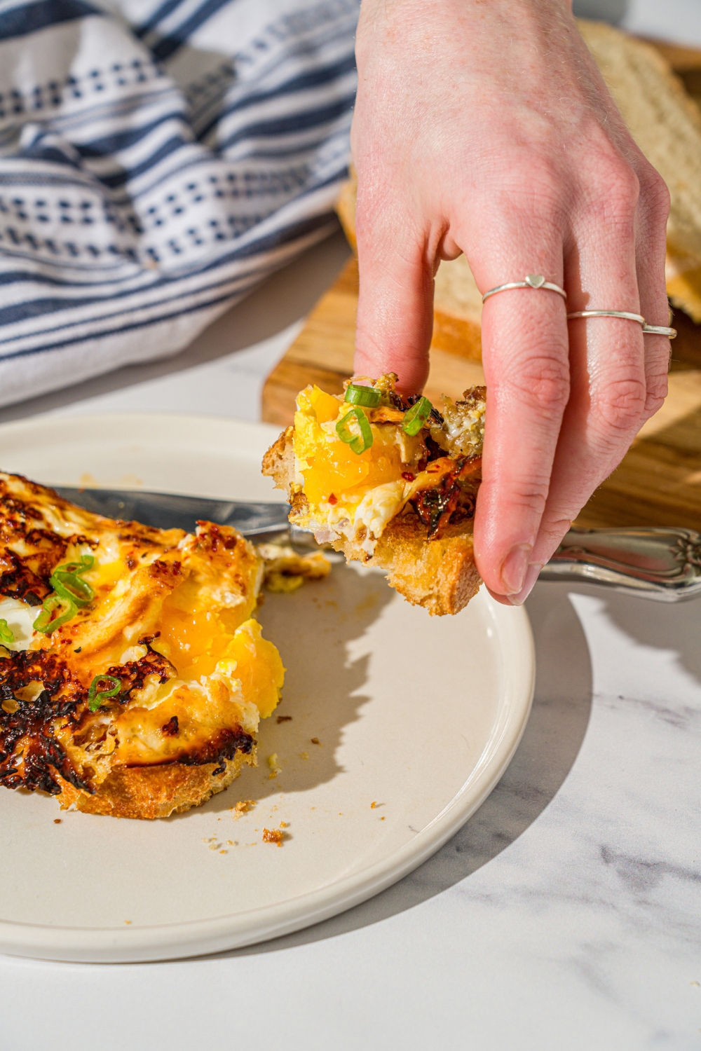 A hand pulling a piece of hot honey eggs on toast away from a slice of the sourdough toast with the hot honey eggs on it.