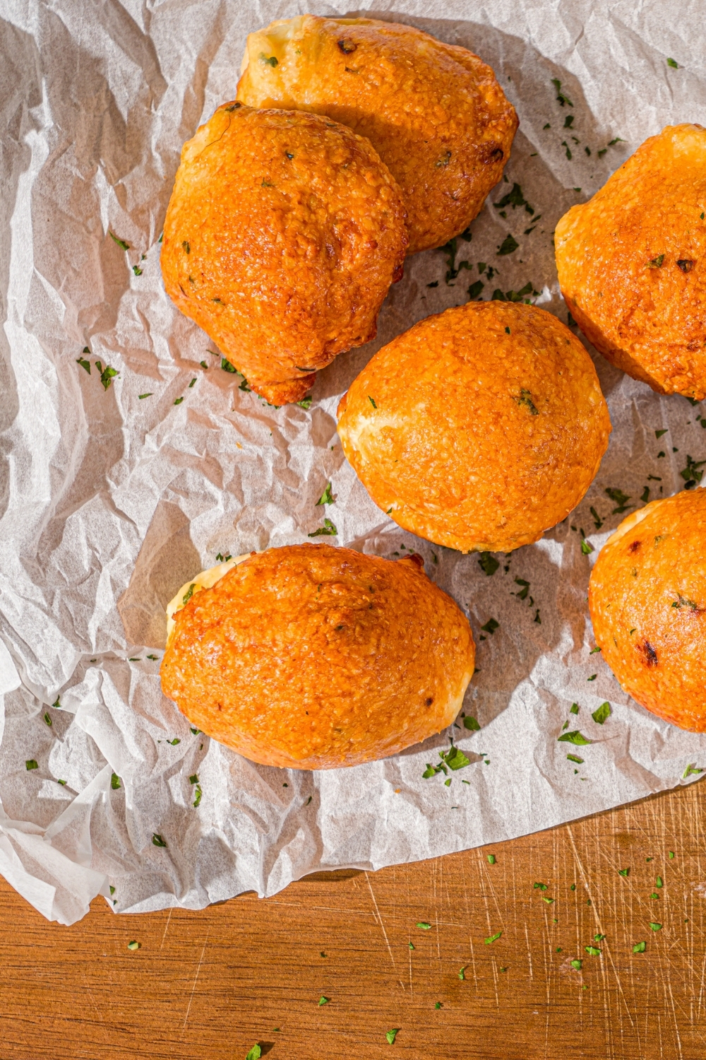 Several air fryer parmesan cheese balls on a piece of parchment paper on a wooden counter garnished with fresh parsley.