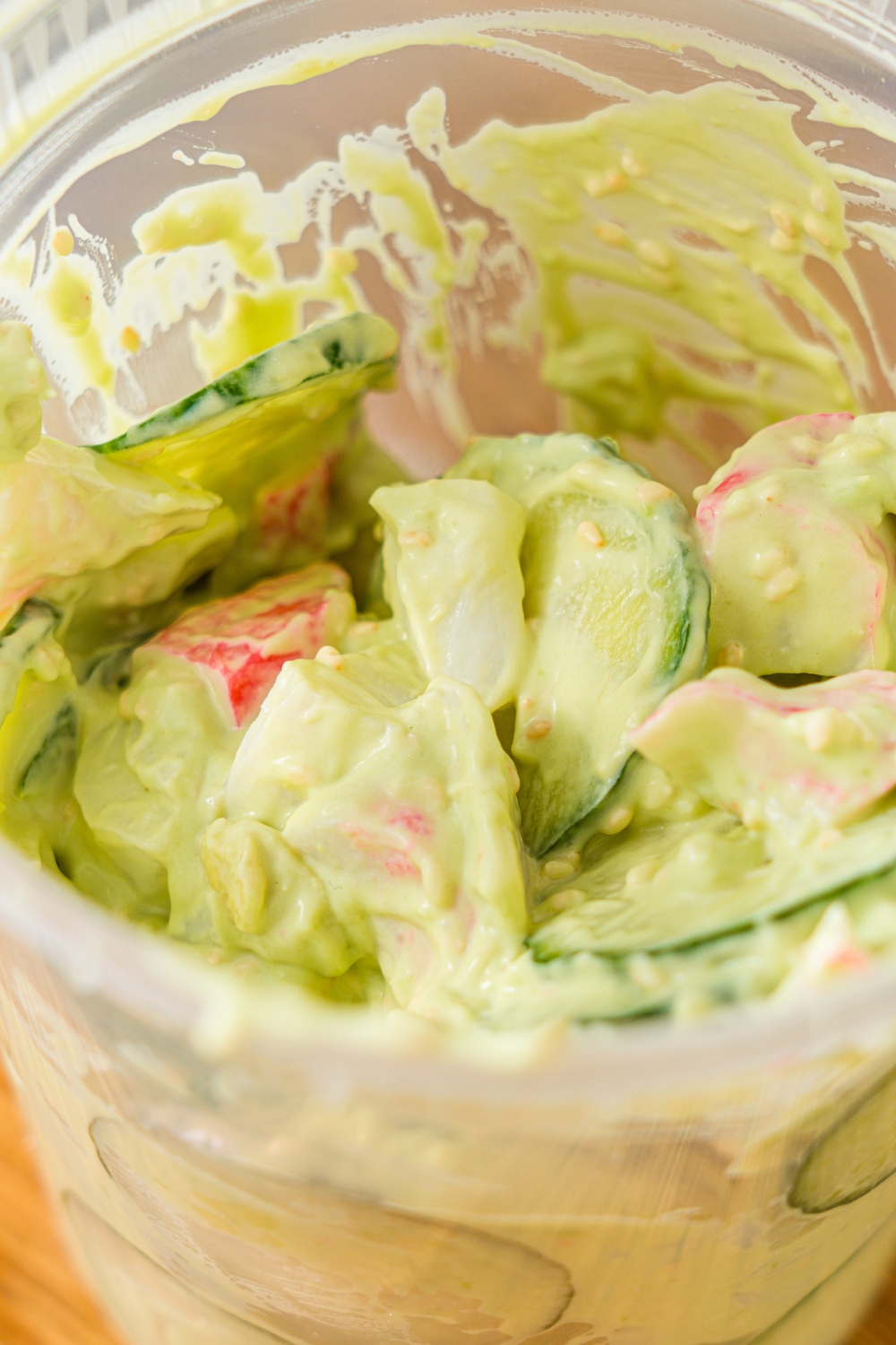 A deli container filled with mixed California roll cucumber salad including sliced cucumber, imitation crab, and sesame seeds in an avocado cream cheese dressing.