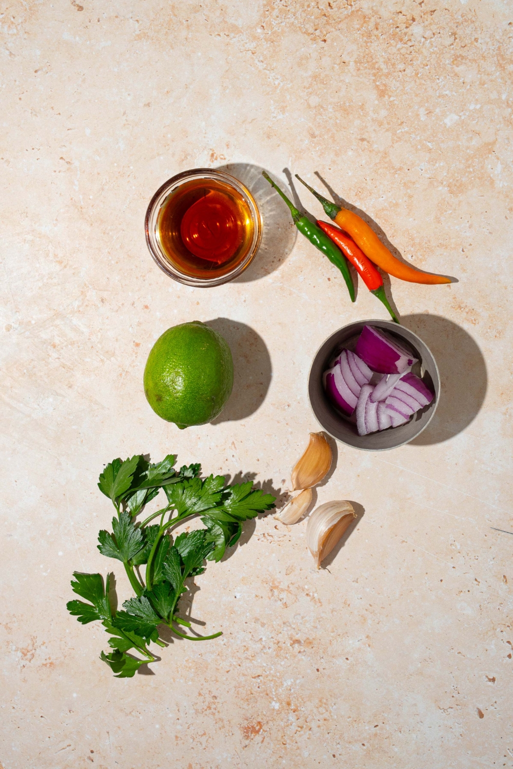 A tan counter with ingredients to make crack sauce including cilantro, red onion, shallot, bird's eye chilis, garlic, and dish sauce.