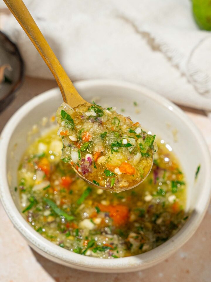 A close up of a spoon with crack sauce. There is a small white bowl of crack sauce on a tan counter blurred in the background.