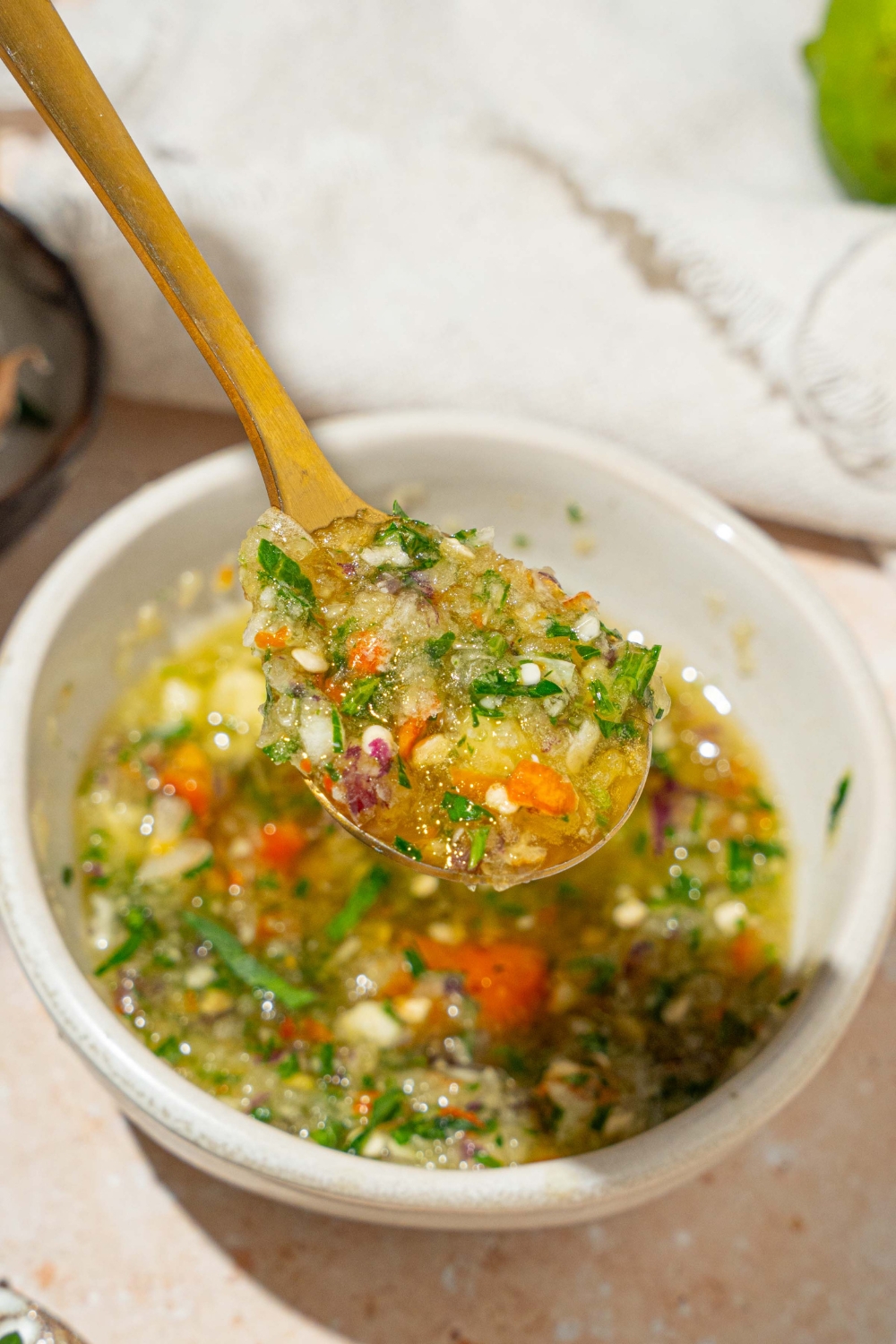 A close up of a spoon with crack sauce. There is a small white bowl of crack sauce on a tan counter blurred in the background.