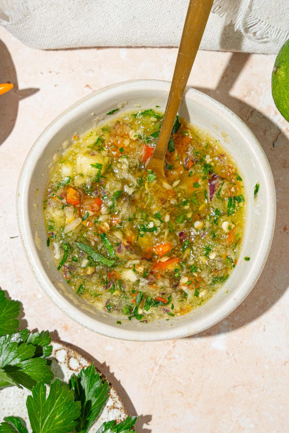 A small white bowl of crack sauce with a spoon in the sauce. The bowl is on a tan counter with a white cloth napkin and cilantro.