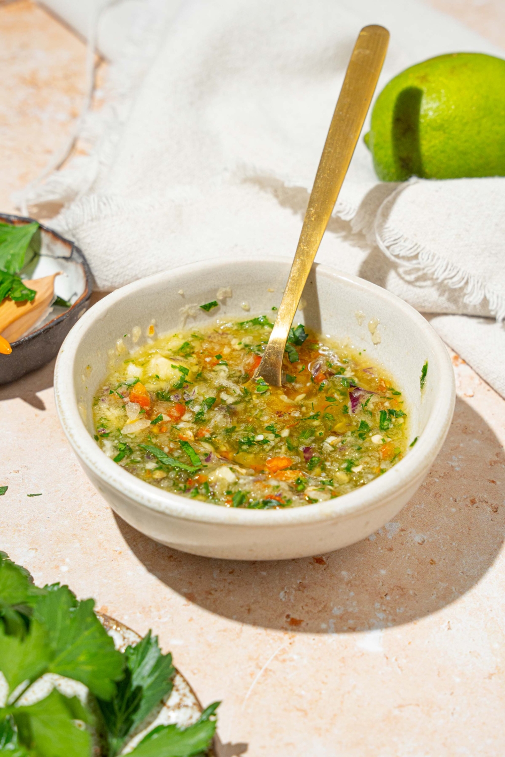 A small white bowl of crack sauce with a spoon in the sauce. The bowl is on a tan counter with a white cloth napkin and lime.
