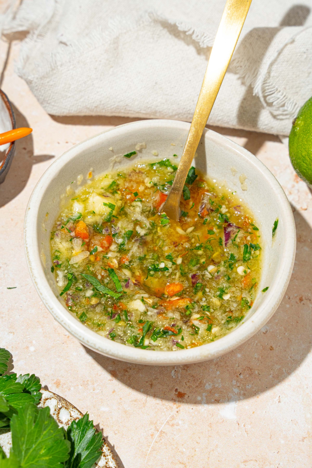 A small white bowl of crack sauce with a spoon in the sauce. The bowl is on a tan counter with a white cloth napkin and lime.