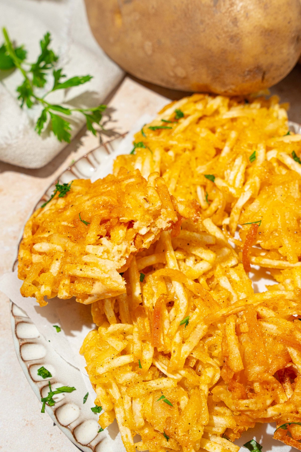 A plate lined with parchment paper with crispy parmesan hashbrowns garnished with fresh parsley. The plate is on a tan counter.