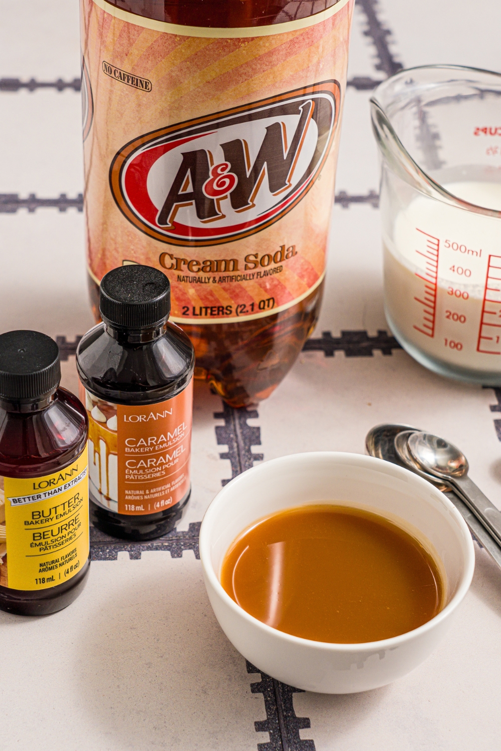 A tiled counter with ingredients to make Harry Potter butterbeer including butterscotch topping, heavy cream, cream soda, butter extract, and caramel extract.