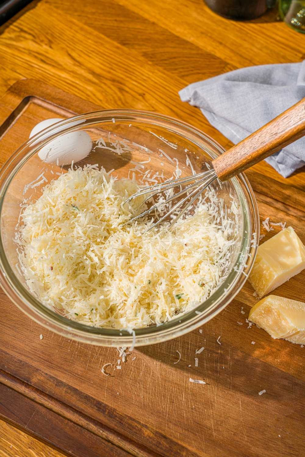 A glass bowl with ingredients to make parmesan cheese ball mixture including parmesan cheese, egg, and seasonings. There is a whisk in the bowl.