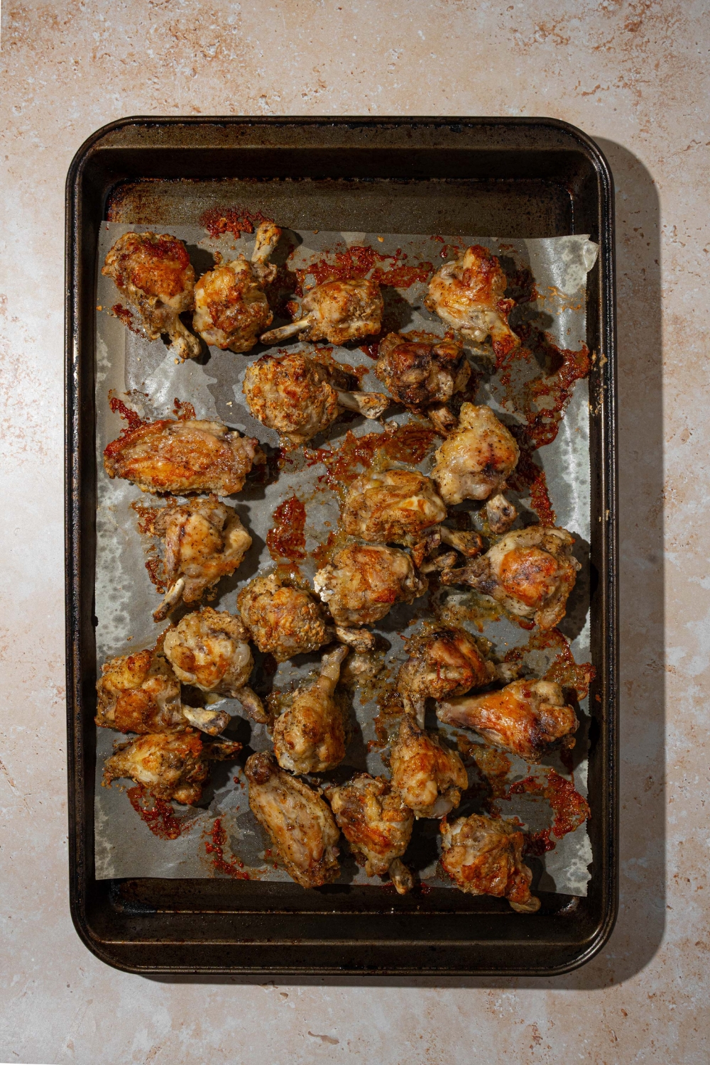 A baking sheet lined with parchment paper with baked chicken wings. The sheet is on a tan counter.