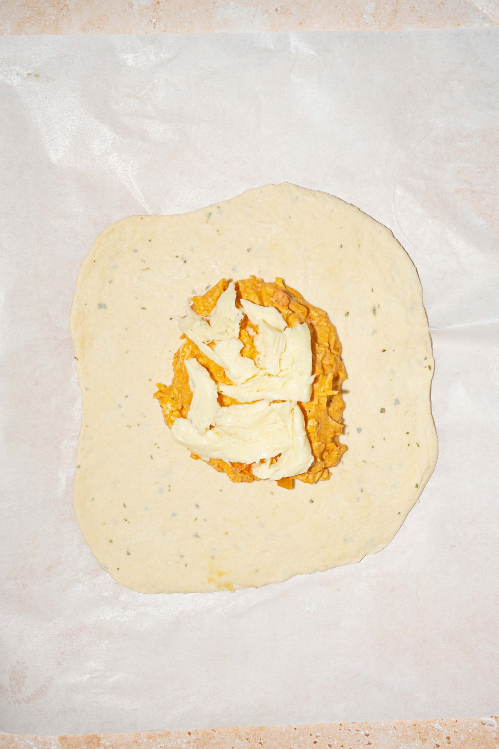 A piece of parchment paper with dough rolled into a rectangle with Buffalo chicken filling in the center of the dough.