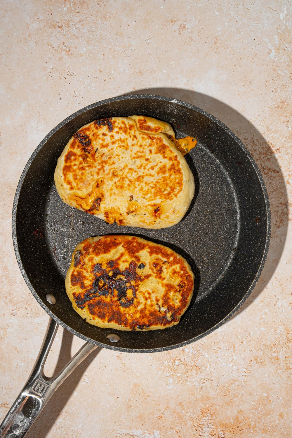A greased skillet with two Buffalo chicken hot pockets. The skillet is on a tan counter.