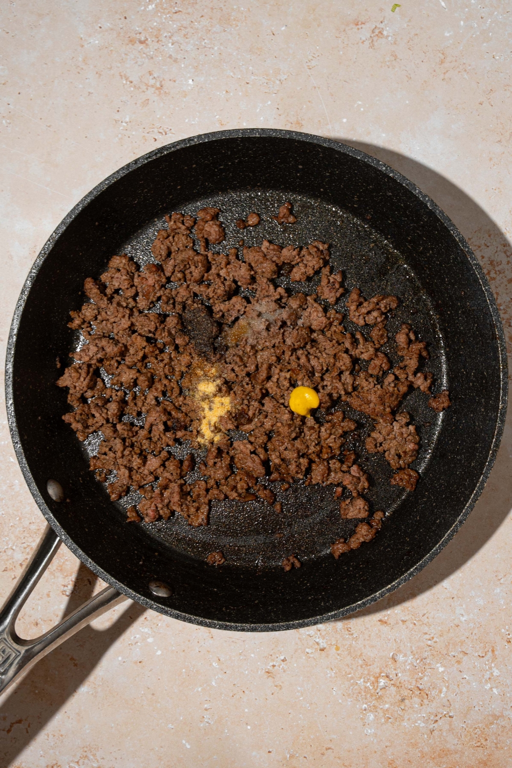 A skillet with ground beef sautéing with seasonings. The skillet is on a tan counter.