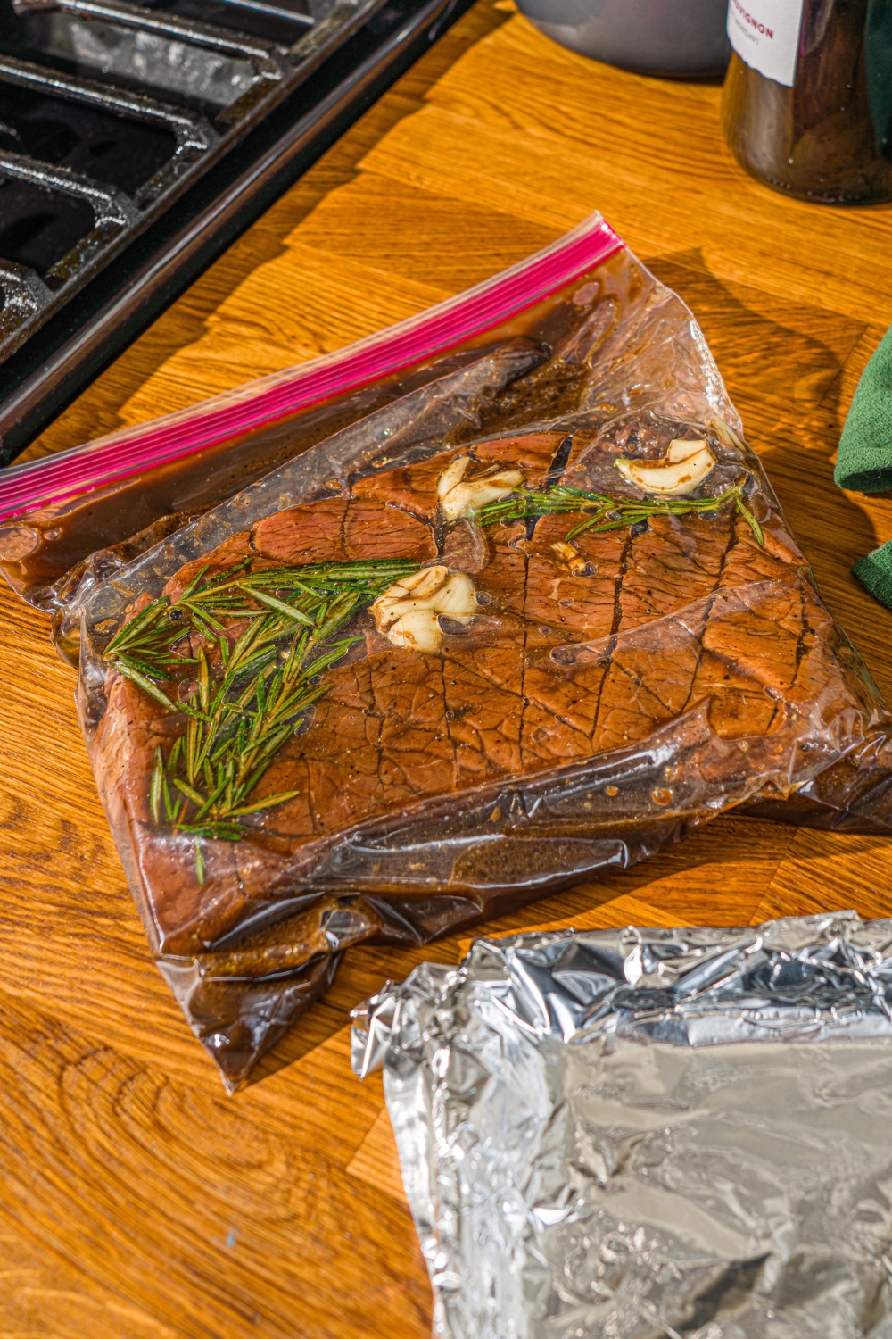 A London broil beef scored in a diagonal pattern in a ziploc bag marinating in London broil marinade. The bag is on a wooden counter.