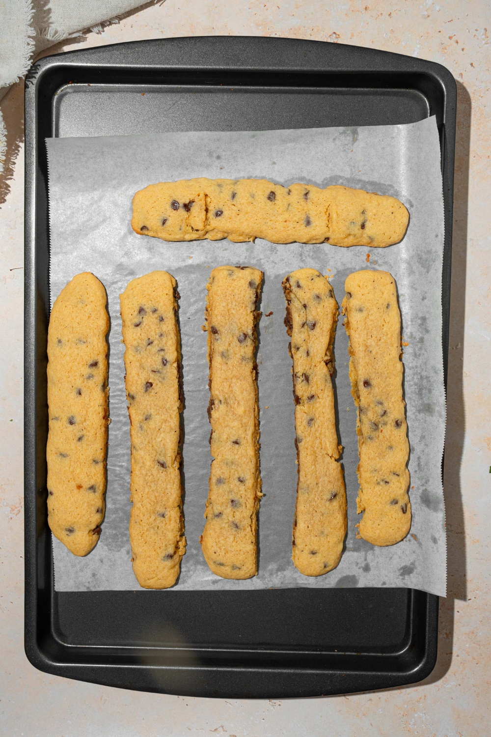 A baking sheet lined with parchment paper with several baked chocolate chip cookie fries. The sheet is on a tan counter.