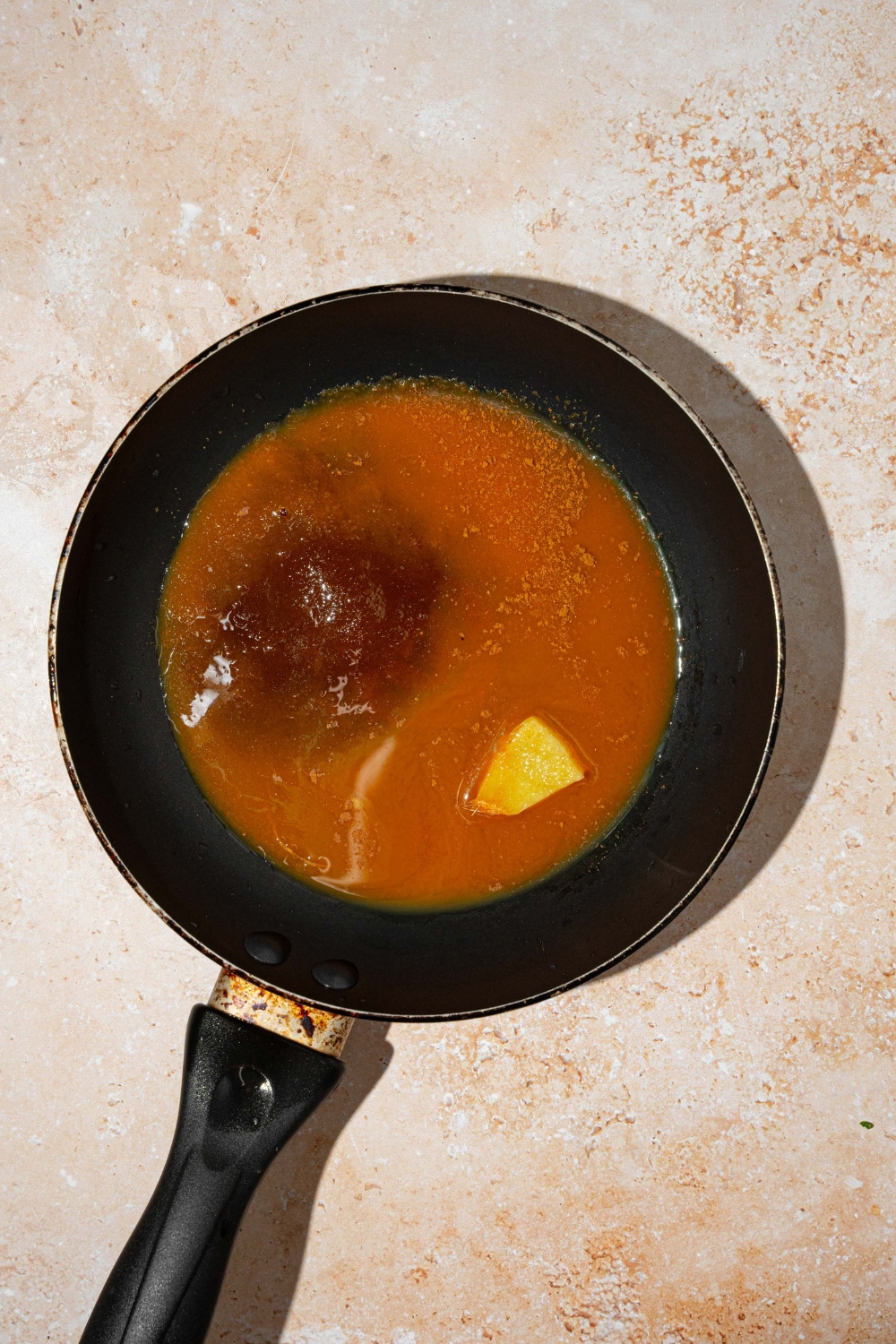 A skillet with ingredients to make carrot cake syrup. The skillet is on a tan counter.