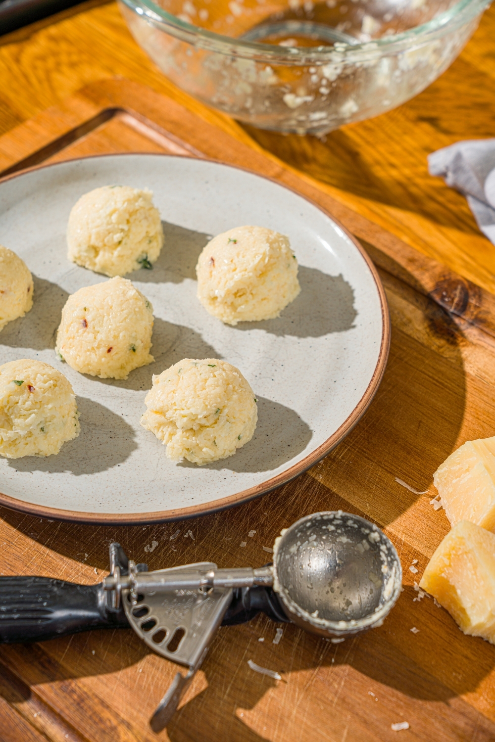 A plate with several scoops of parmesan cheese ball mixture. The plate is on a wooden board with a mini scooper and parmesan cheese.