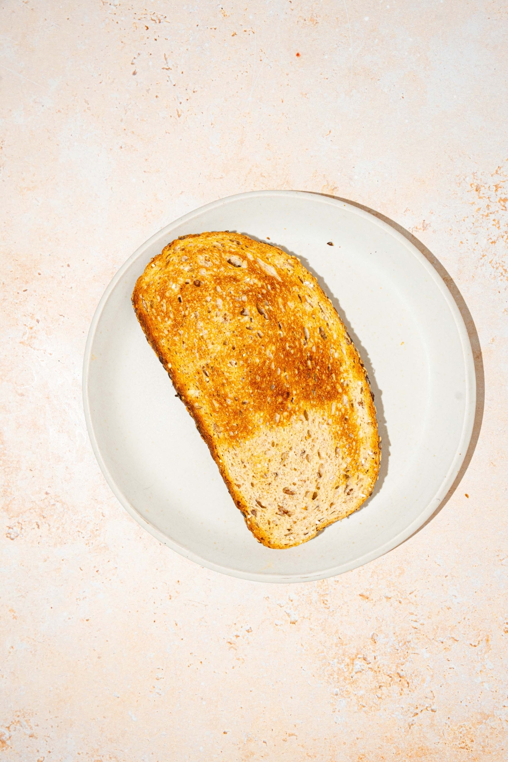 A white plate with a slice of toast. The plate is on a tan counter.