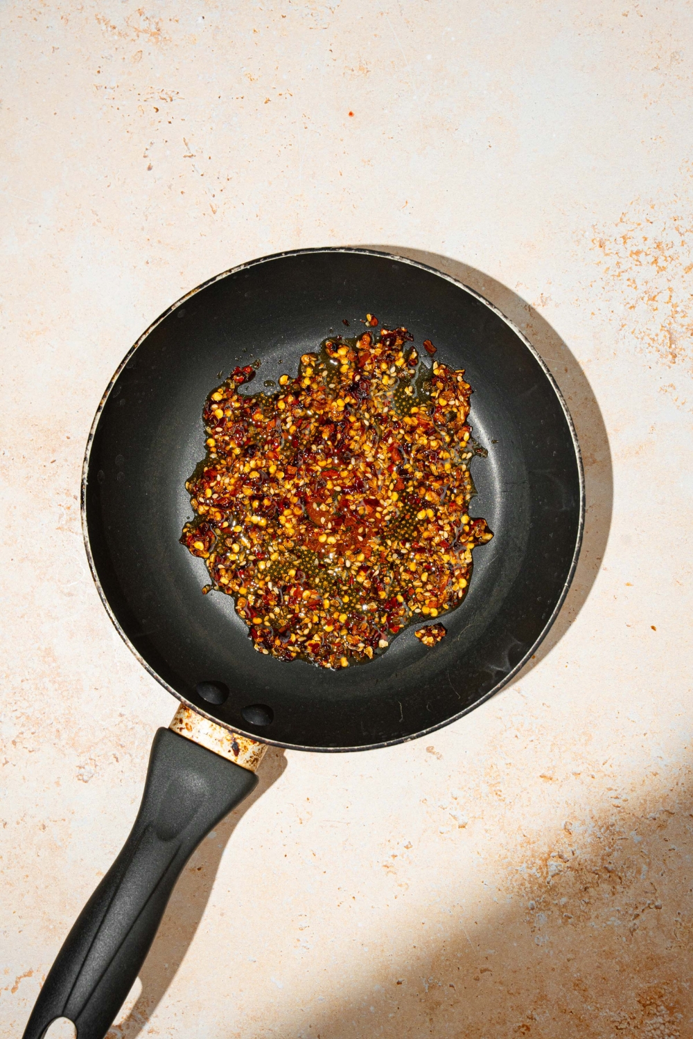 A skillet with chili crisp oil. The skillet is on a tan counter.
