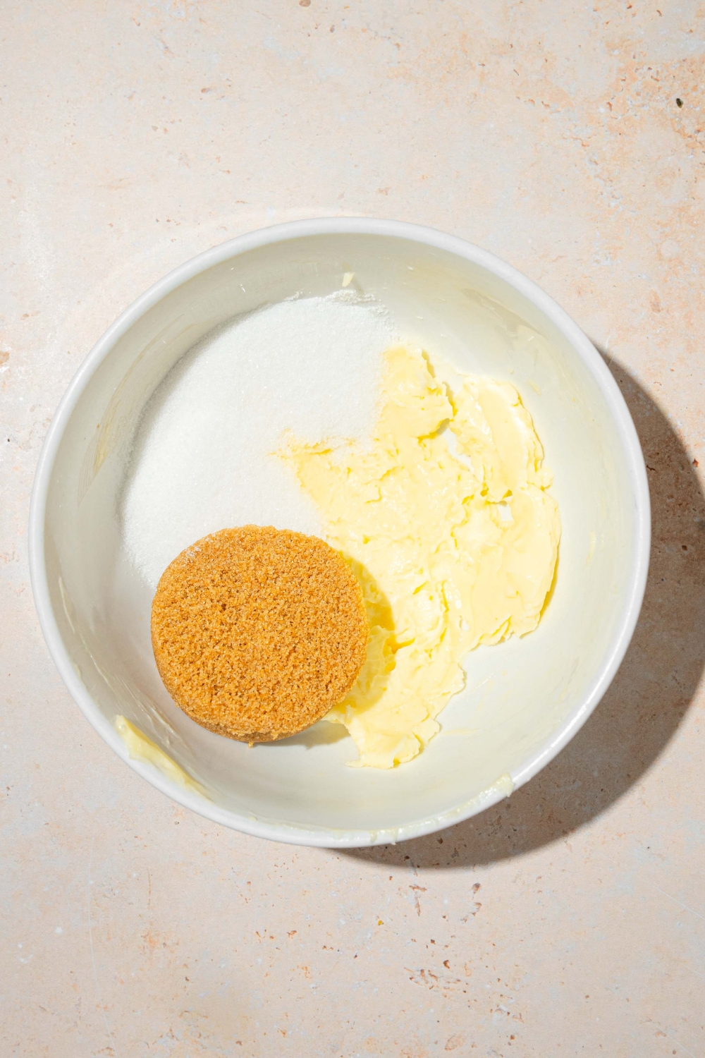 A large white bowl with ingredients to make chocolate chip cookie fries dough including brown sugar, butter, and sugar.